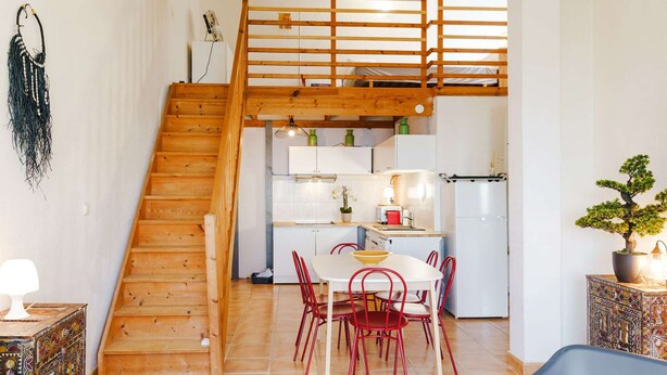 A wooden staircase leading to a kitchen with white cabinets, a dining table with red chairs, and a potted bonsai tree. - A/C T2 Mezzanine, 6 Guests - Plage des Chalets, Gruissan (Gruissan)