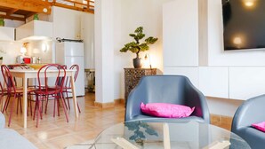 Un salón moderno con una mesa de centro de vidrio, sillas rojas y un sofá azul con un cojín rosa.
