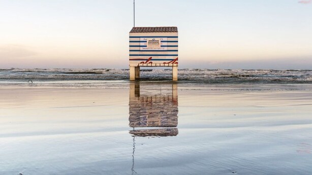 Una torre de socorrista en la playa, con diseño a rayas y un asta de bandera.