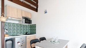 A compact kitchen with a microwave, stove, and a small refrigerator. There is a dining table with four chairs and a small sink. - Loft Studio for 4, Sea View, Comfort in Saint Pierre La Mer (Fleury-Saint-Pierre-la-Mer)