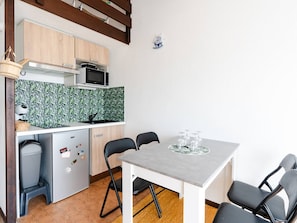A compact kitchen with a microwave, stove, and a small refrigerator. There is a dining table with four chairs and a small sink. - Loft Studio for 4, Sea View, Comfort in Saint Pierre La Mer (Fleury-Saint-Pierre-la-Mer)