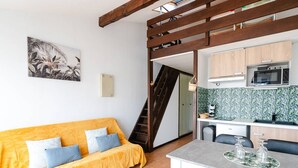 A compact living space with a sofa, a dining table, a kitchen area, and a staircase. - Loft Studio for 4, Sea View, Comfort in Saint Pierre La Mer (Fleury-Saint-Pierre-la-Mer)