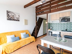A compact living space with a sofa, a dining table, a kitchen area, and a staircase. - Loft Studio for 4, Sea View, Comfort in Saint Pierre La Mer (Fleury-Saint-Pierre-la-Mer)
