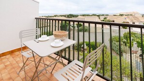 A balcony with a table set for two, chairs, and a wicker basket. - Loft Studio for 4, Sea View, Comfort in Saint Pierre La Mer (Fleury-Saint-Pierre-la-Mer)