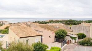 A coastal residential area with terracotta-tiled roofs, a paved street, and a view of the sea. - Loft Studio for 4, Sea View, Comfort in Saint Pierre La Mer (Fleury-Saint-Pierre-la-Mer)