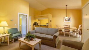 Ein Wohnzimmer mit einer Couch, einem Esstisch, Stühlen, einer Lampe und einem kleinen Tisch mit einer Pflanze.
