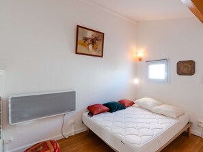 A bedroom with a bed, a radiator, a wall-mounted light, a window, and a painting. - Charming 2BR Cottage with Pool, Terrace & Parking Near Beach (Gruissan)