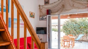 Escada que leva a um sofá vermelho, uma televisão e uma porta de vidro deslizante para um pátio externo com uma mesa e cadeiras.