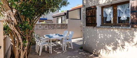 An outdoor patio with a table and chairs, a tree, and a building with a window.