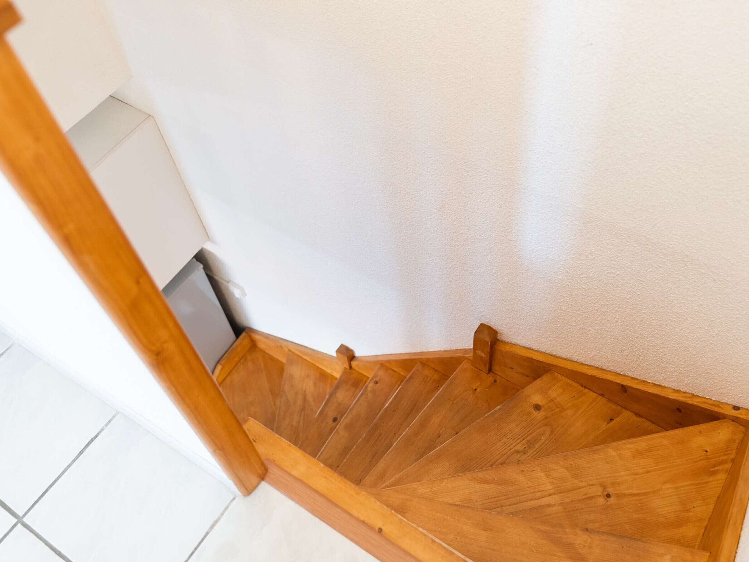 Una escalera de madera con una pared blanca y suelo de baldosas.