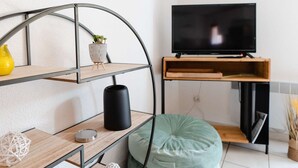 Ein modernes Wohnzimmer mit einer gebogenen Metallregalwand, einem Flachbildfernseher auf einem Holzbodenständer, einem grünen Sitzsack und einem kleinen Topfpflanzen.