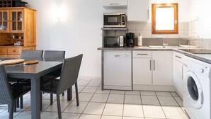 Eine kompakte Küche mit Essbereich, darunter ein Tisch mit Stühlen, eine Mikrowelle, eine Kaffeemaschine und eine Waschmaschine.