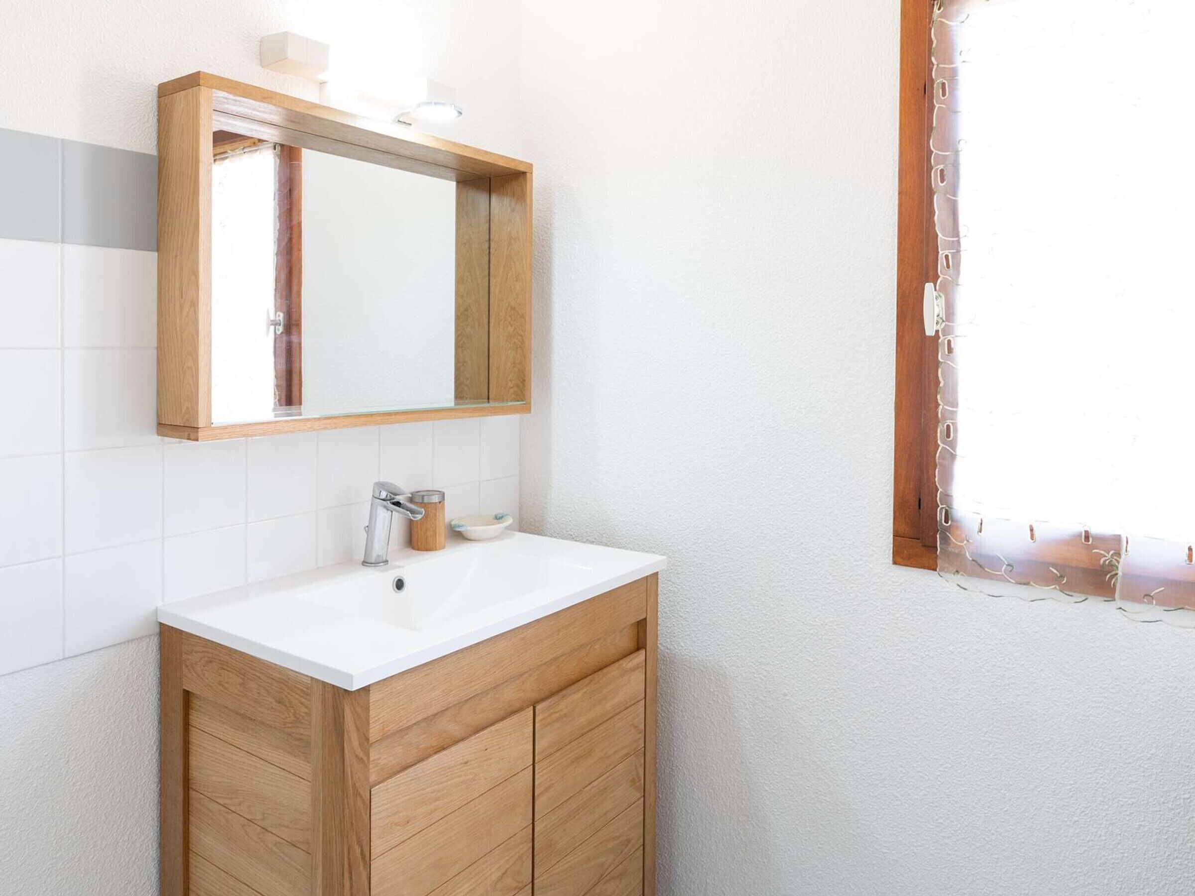 Bany amb un envà d'estil rústic, un lavabo blanc, un mirall i una finestra amb cortina.