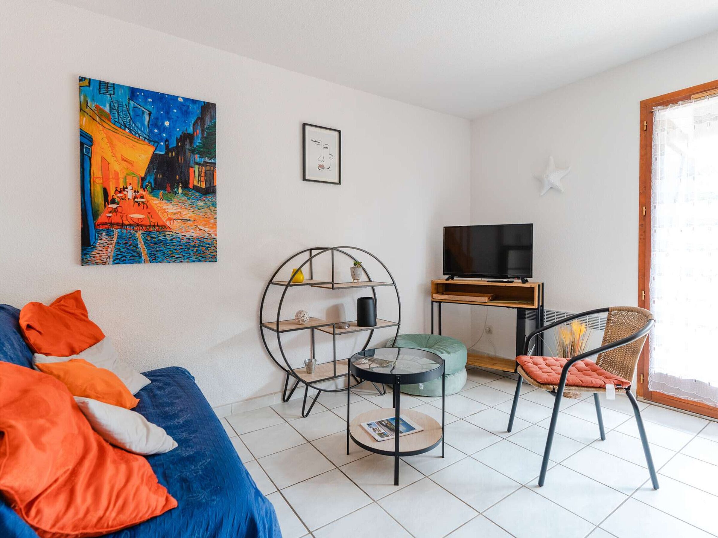 A living room with a blue sofa, a round coffee table, a TV stand, and a chair.