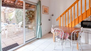A dining area with a table and chairs, a wooden staircase, and a sliding glass door leading to an outdoor patio. - Air-conditioned 3-Room Cottage with Mezzanine and Terrace, 200m from Narbonne Beach – Sleeps 6 (Narbonne-Narbonne Plage-Narbonne Plage)