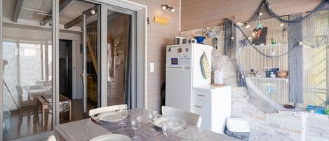 Un comedor con una mesa dispuesta para cuatro personas, un refrigerador y una zona de cocina con una red colgante.