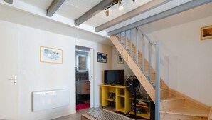 Ein modernes Wohnzimmer mit einer Holzbank, einem Fernseher auf einem gelben Standfuß und einer Treppe mit einer Holzwandung.