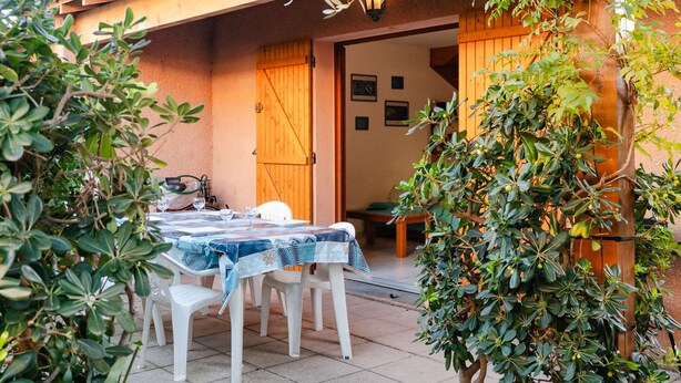 An outdoor patio with a table and chairs, a wooden door, and a small garden area.