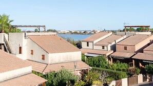 A residential area with terracotta-tiled roofs, a clear blue sky, and a body of water in the background.