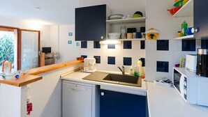 A compact kitchen with a dishwasher, a sink, and a microwave. There is a wooden counter and a shelf with dishes and cups.