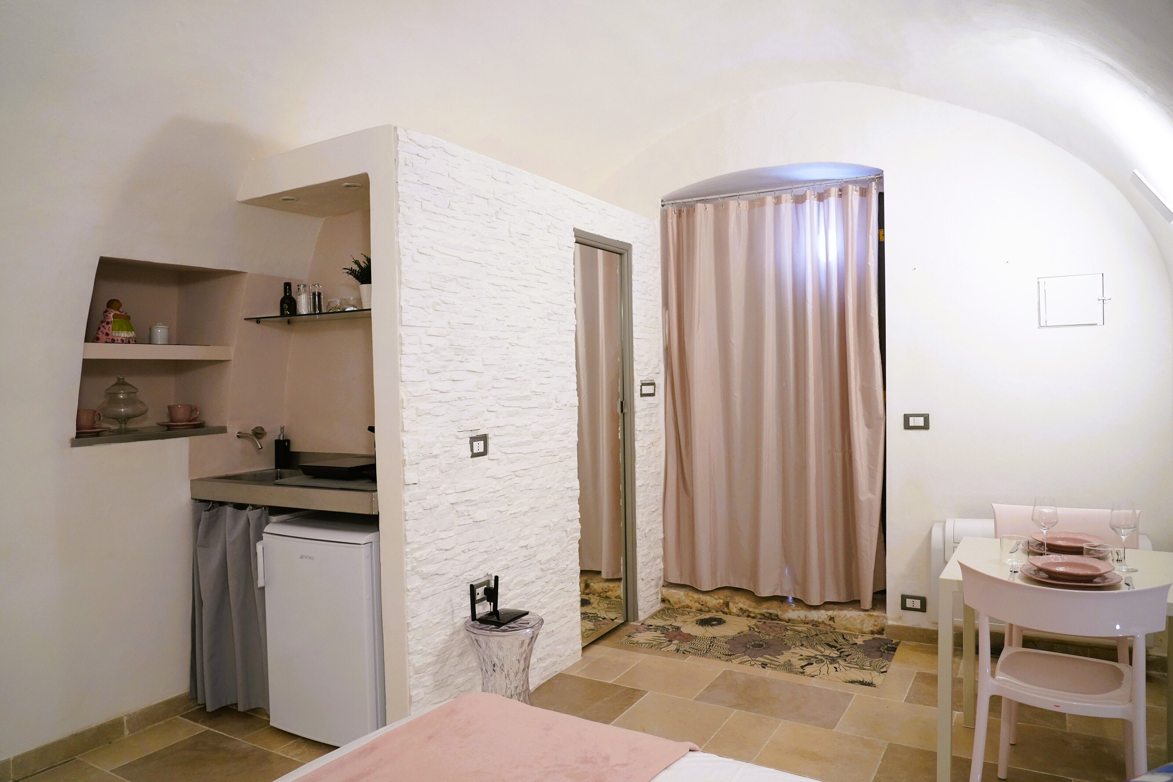 A compact room with a kitchenette, a small table with chairs, a mirror, and a curtain.