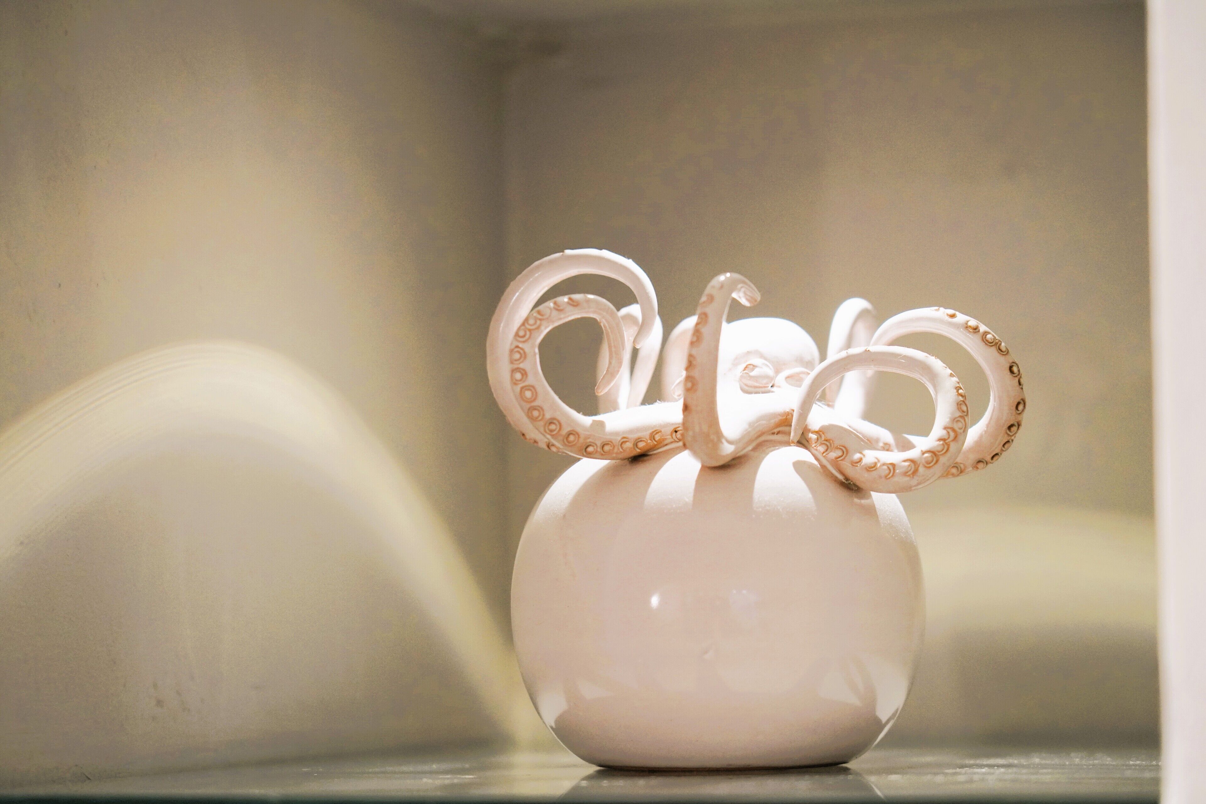 A white ceramic vase with octopus tentacles on a shelf.