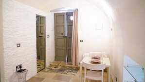 A room with a white brick wall, a glass door, a small table with a chair, and a glass cabinet. - La Chianca Rosa - Arcuève (Ostuni)