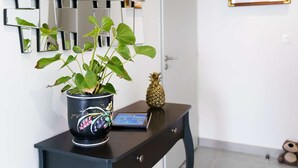 A room with a dark wooden console table, a potted plant, a pineapple, and a framed picture on the wall. - Modern 2-bedroom apt, air-con, 2 parking spots, 300m from beach (Narbonne-Narbonne Plage-Narbonne Plage)