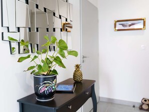 Ein Zimmer mit einer dunklen Holztruhe, einem Topfpflanzen, einer Ananas und einem gerahmten Bild an der Wand.
