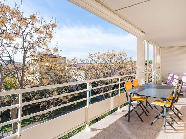Ein Balkon mit Tisch und Stühlen, Blick auf Bäume und Gebäude sowie einer Brüstung.