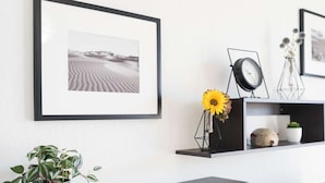 Un salon moderne avec une photographie encadrée représentant un paysage désertique, une plante en pot, un vase avec des tournesols, une horloge et des objets décoratifs disposés sur des étagères.