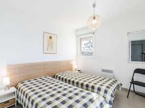 Une chambre avec deux lits, une fenêtre, un luminaire suspendu, un tableau encadré au mur et une chaise.