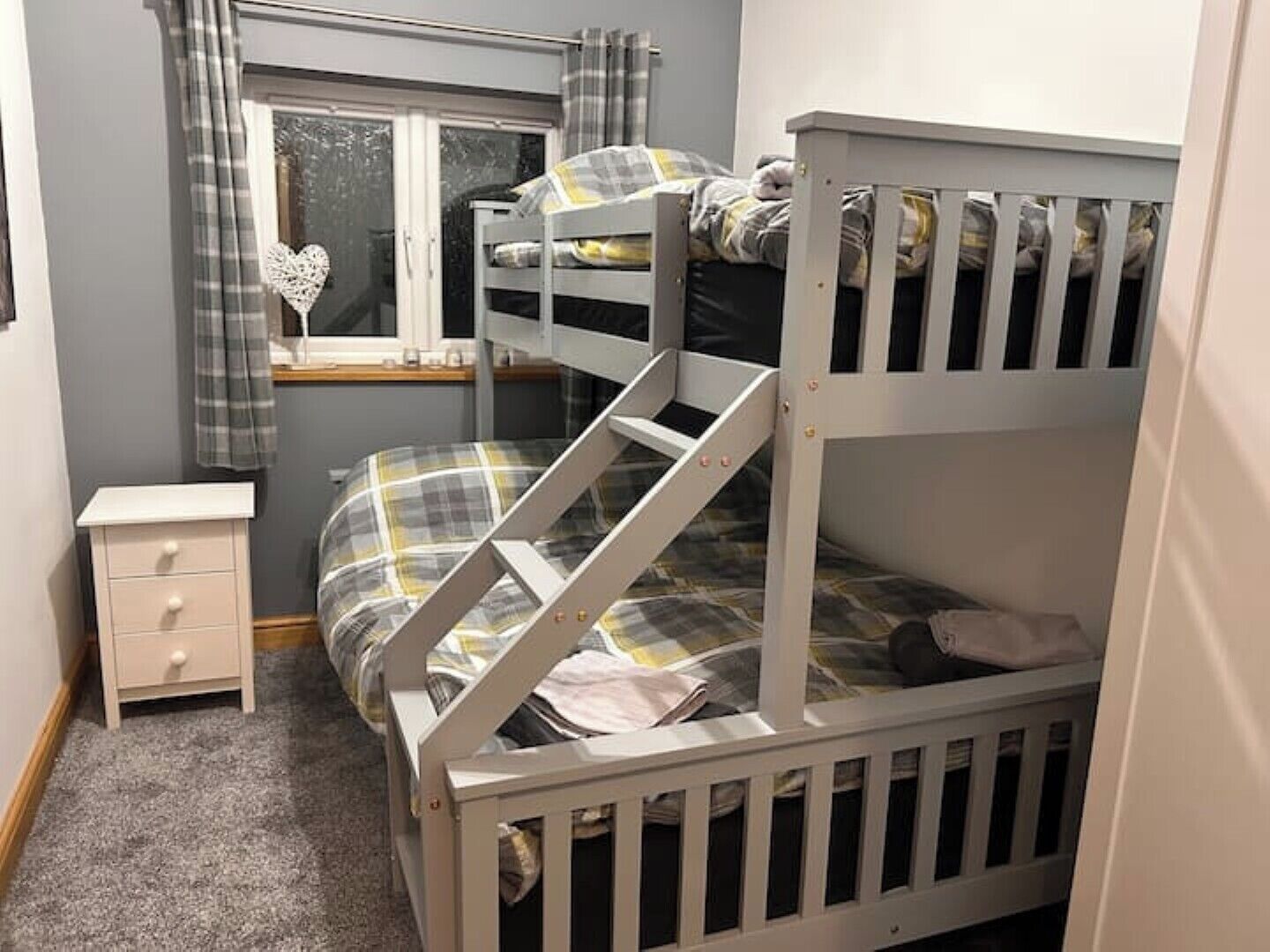 A bunk bed with a window, a bedside table, and a heart-shaped decoration.