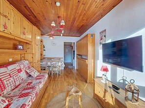 Ein gemütliches Wohnzimmer mit Holzboden, einer Couch mit gemustertem Bezug, einem Esstisch mit Stühlen und einem Fernseher an der Wand.