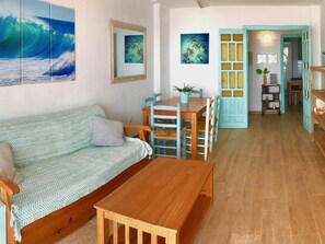 Ein gemütlicher Wohnbereich mit einer Couch, einem Holztisch und einem Esstisch mit Stühlen. An den Wänden hängen gerahmte Bilder und eine Tür mit einem dekorativen Zierfeld.