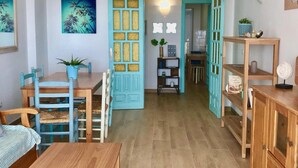 Ein Zimmer mit einem Holztisch, Stühlen, einer blauen Tür mit dekorativer Zarge, einem Wandregal und einem Deckenventilator.