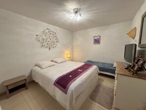 Une chambre à coucher comprenant un lit, une table de chevet, une lampe, un téléviseur et un élément décoratif mural.