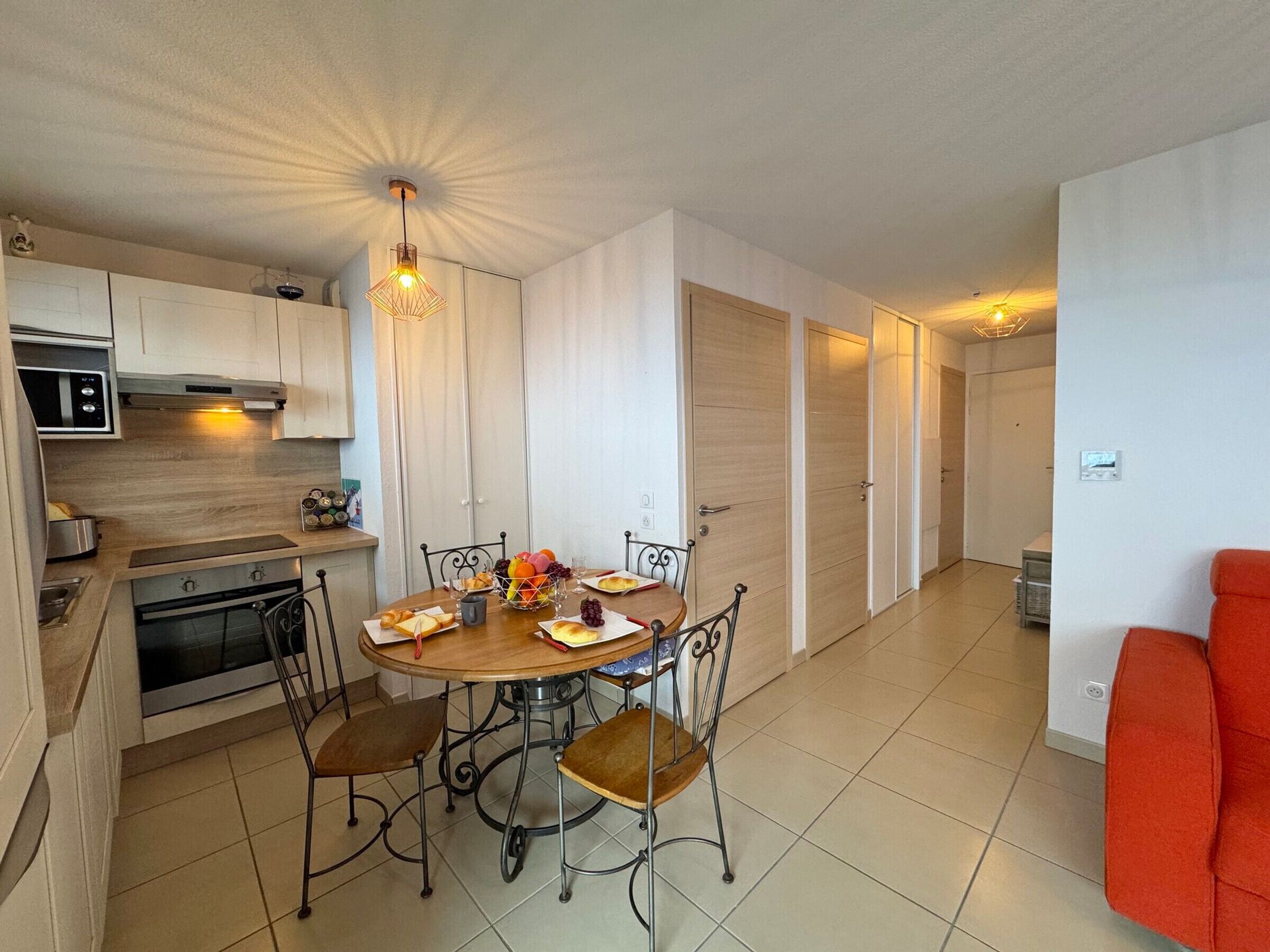 Una cucina compatta con elettrodomestici moderni, un'area pranzo con un tavolo rotondo e sedie, e una lampada a sospensione luminosa.