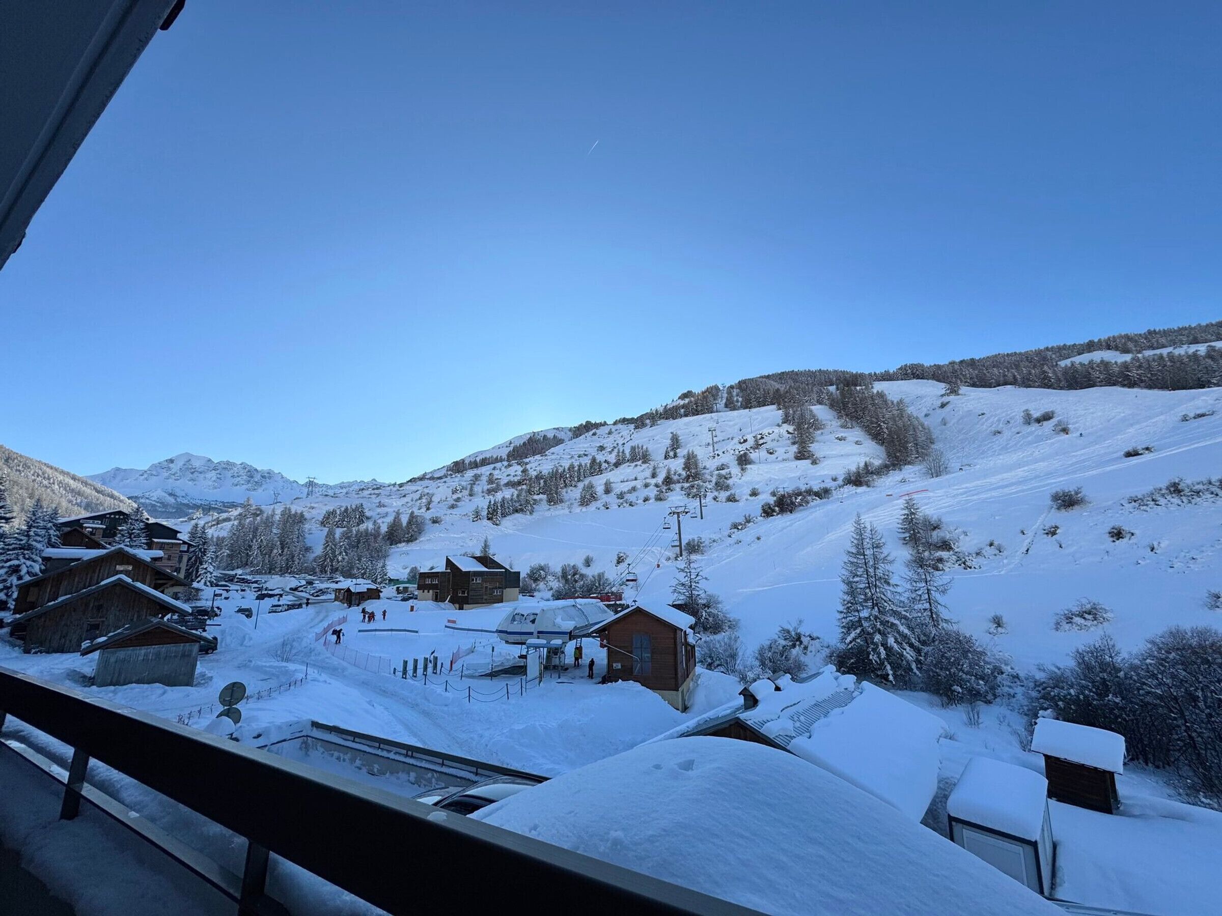 En snötäckt bergsby med trähus, en skidlift och en klarblå himmel.