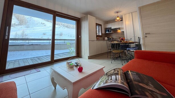 Quarto aconchegante com área de jantar, cozinha e grande janela com vista para uma paisagem coberta de neve.