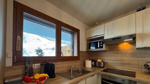 Uma cozinha moderna com bancadas de madeira, forno embutido, micro-ondas e uma janela com vista para uma paisagem nevada.
