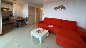 Uma sala de estar moderna com um sofá vermelho, uma mesa de centro branca e uma área de jantar com mesa e cadeiras.