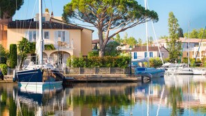 A marina with boats docked, a large tree in the center, and buildings with balconies. - Beachfront Studio with A/C and Parking in Port Grimaud (Port Grimaud)