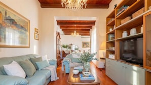 A living room with a sofa, coffee table, TV, and wooden shelves. - ClickSardegna – Elegant historic palace with sea view in the old town, with lift (Alghero)