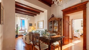 A dining area with a wooden table set for four, surrounded by chairs. A large wooden cabinet with glass doors is visible in the background. - ClickSardegna – Elegant historic palace with sea view in the old town, with lift (Alghero)