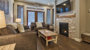 A modern living room with a fireplace, a sofa, a coffee table, and a television mounted above the fireplace. - Bottom Floor, Walk Out Condo with great ski access and private hot tub! (Sun Peaks)