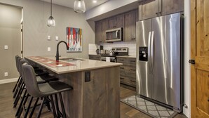 A modern kitchen with a central island, stainless steel appliances, and bar stools. - Bottom Floor, Walk Out Condo with great ski access and private hot tub! (Sun Peaks)