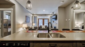 A modern kitchen with a large island, double sink, and pendant lighting. - Bottom Floor, Walk Out Condo with great ski access and private hot tub! (Sun Peaks)