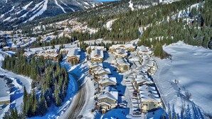 A snow-covered resort with multiple chalet-style buildings, a ski slope, and a frozen lake. - Bottom Floor, Walk Out Condo with great ski access and private hot tub! (Sun Peaks)