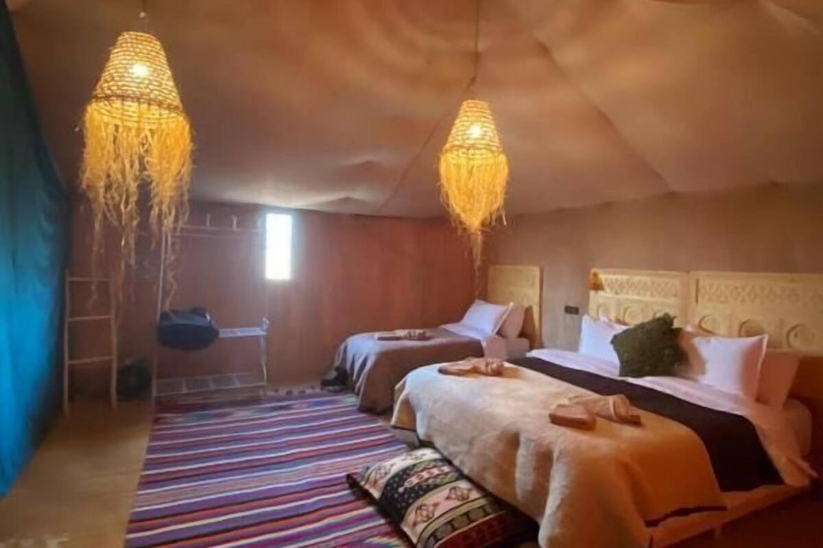 A cozy room with a sloped ceiling, two beds with colorful bedding, a hanging light fixture, and a striped rug.